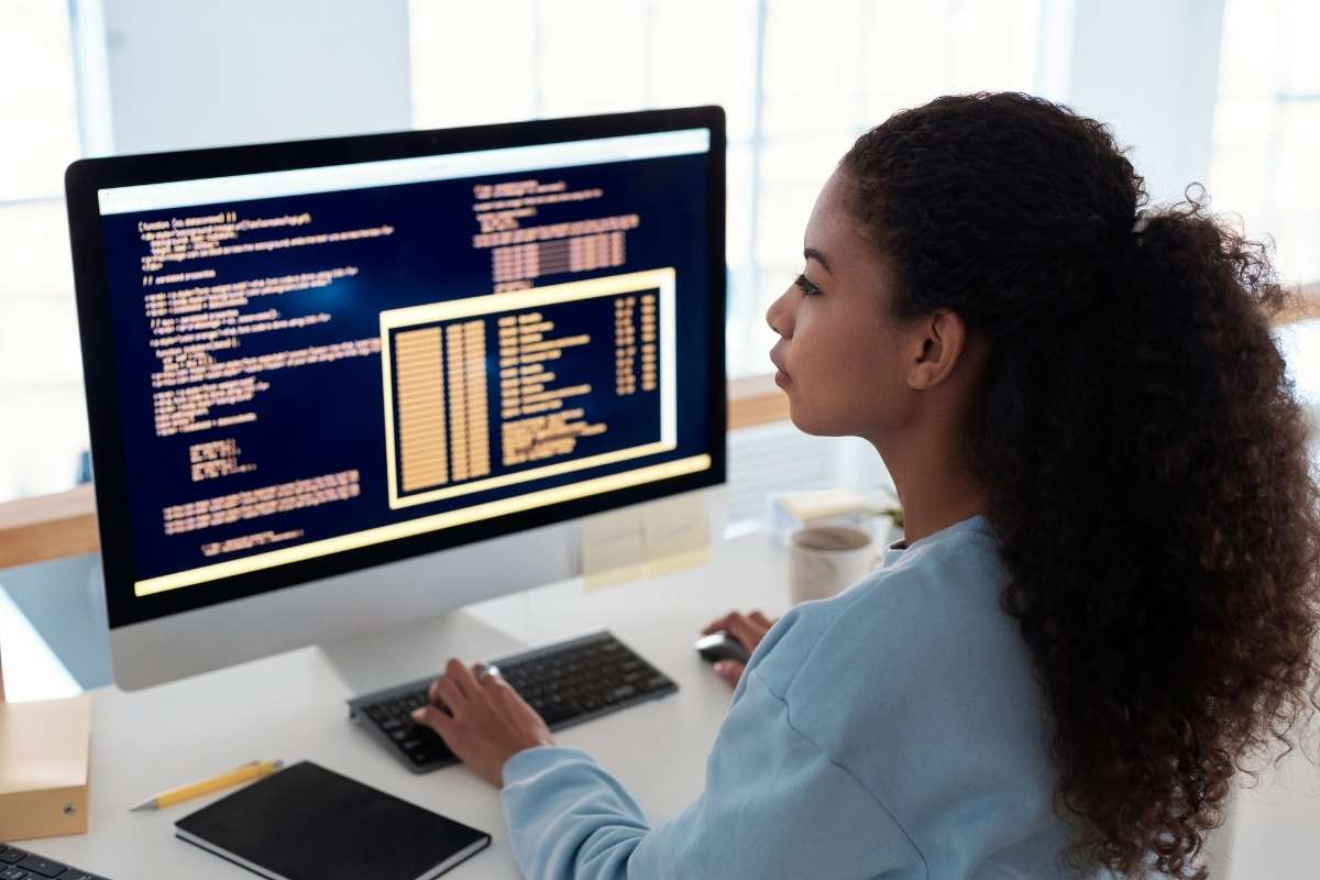 Une femme travaille devant un écran d'ordinateur affichant du code, illustrant les tests automatisés en développement.